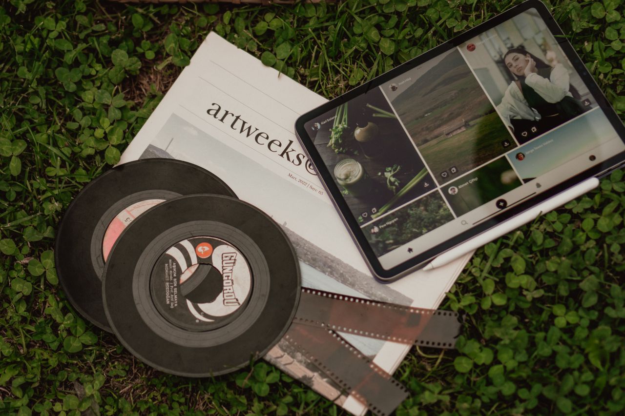 A flat lay of vintage films, a newspaper, and a tablet on grass.