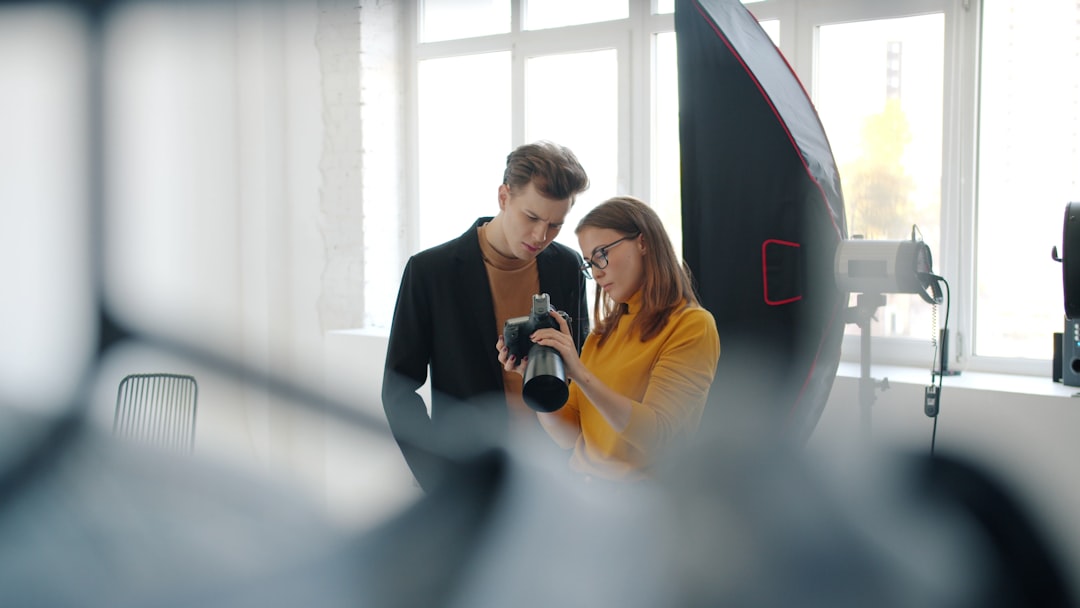 Girl and guy model are talking in photo studio watching pictures on digital camera standing indoors together communicating after photo shoot. Youth and technology concept.